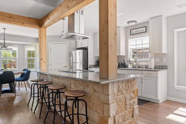 kitchen featuring wood finished floors, island range hood, black electric cooktop, white cabinetry, and freestanding refrigerator