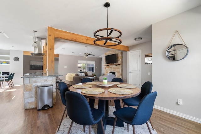 dining space with ceiling fan with notable chandelier, baseboards, wood finished floors, and a fireplace