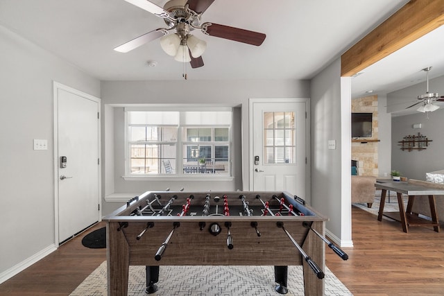rec room with baseboards, a stone fireplace, wood finished floors, and ceiling fan