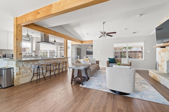 living area featuring lofted ceiling, wood finished floors, visible vents, a fireplace, and ceiling fan