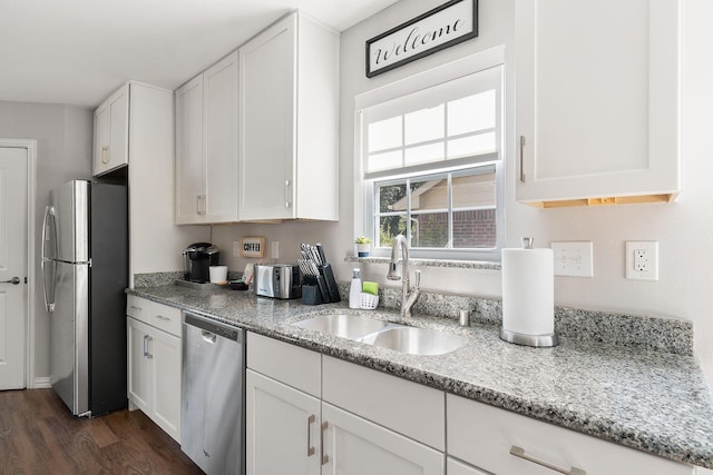 kitchen with a sink, white cabinets, appliances with stainless steel finishes, light stone countertops, and dark wood-type flooring