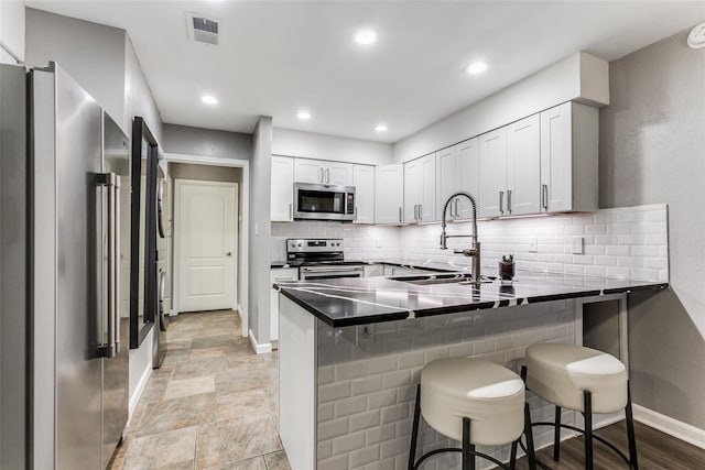 kitchen with stainless steel appliances, a sink, baseboards, a peninsula, and tasteful backsplash