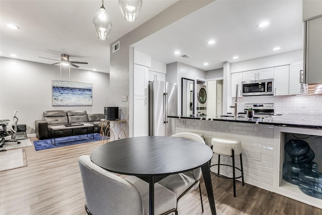 kitchen with stacked washer / drying machine, stainless steel appliances, visible vents, a peninsula, and white cabinetry