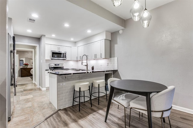 kitchen with stainless steel appliances, a peninsula, a sink, baseboards, and decorative backsplash