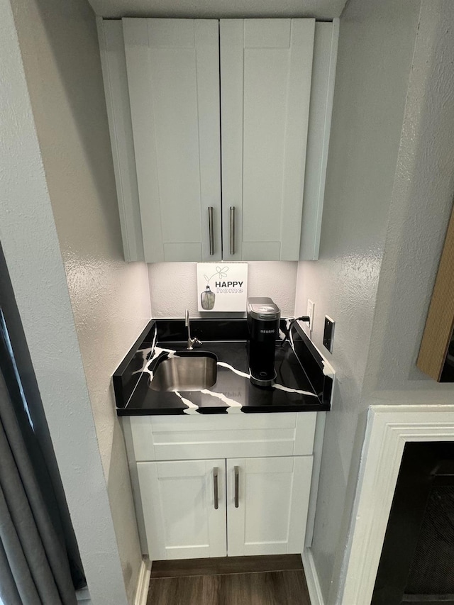 laundry area featuring dark wood finished floors, baseboards, a textured wall, and a sink