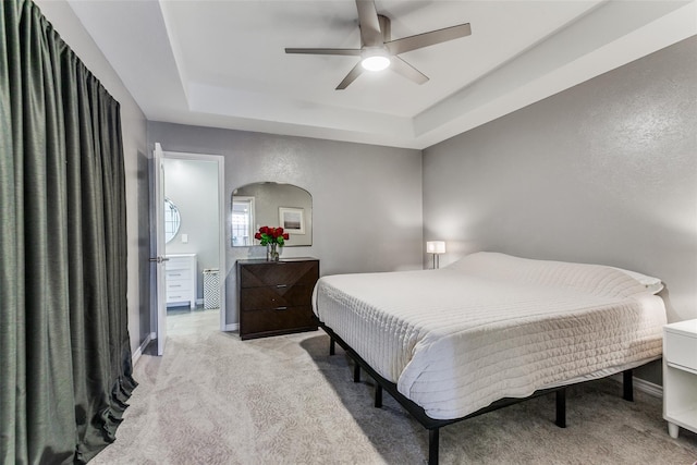 bedroom with light carpet, a ceiling fan, a tray ceiling, and baseboards