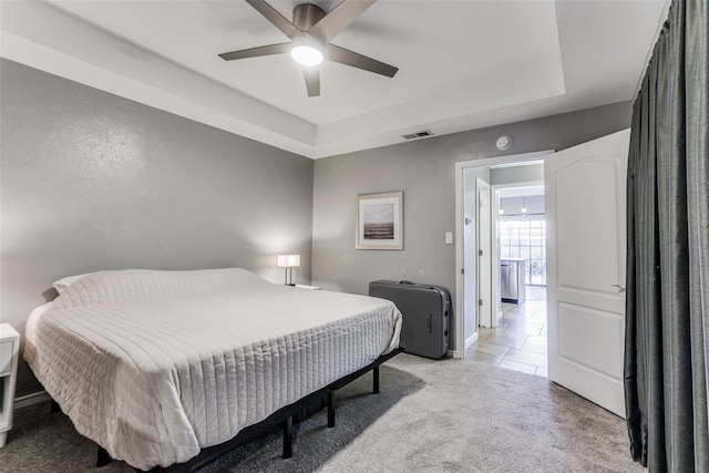 bedroom featuring a ceiling fan, light carpet, a tray ceiling, baseboards, and visible vents