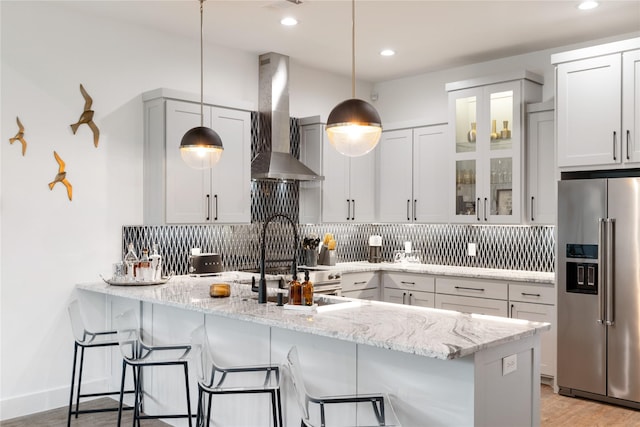 kitchen with wall chimney range hood, tasteful backsplash, high quality fridge, and a breakfast bar area