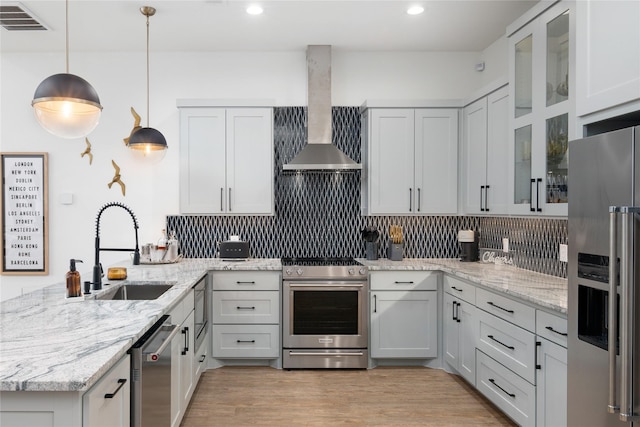 kitchen with a sink, a peninsula, wall chimney exhaust hood, backsplash, and stainless steel appliances