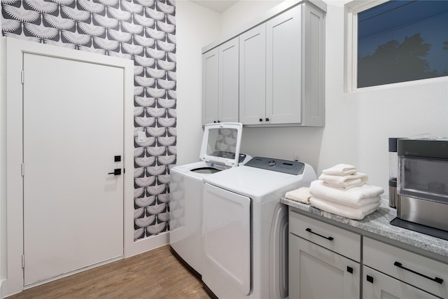 washroom with separate washer and dryer, cabinet space, and light wood-style floors