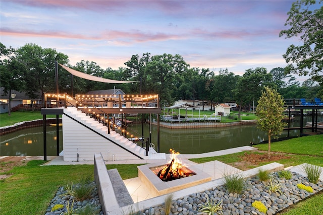 surrounding community with a water view, a fire pit, and a lawn