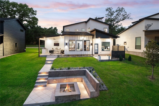 back of property at dusk with a yard, board and batten siding, a patio area, and an outdoor living space with a fire pit