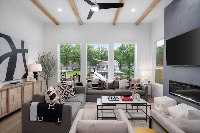 living room with a ceiling fan, a healthy amount of sunlight, beam ceiling, and wood finished floors