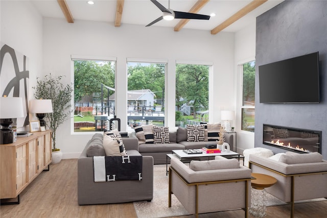 living area with beam ceiling, light wood-style flooring, and ceiling fan