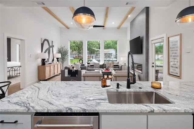 kitchen with light stone countertops, beam ceiling, a sink, and wood finished floors
