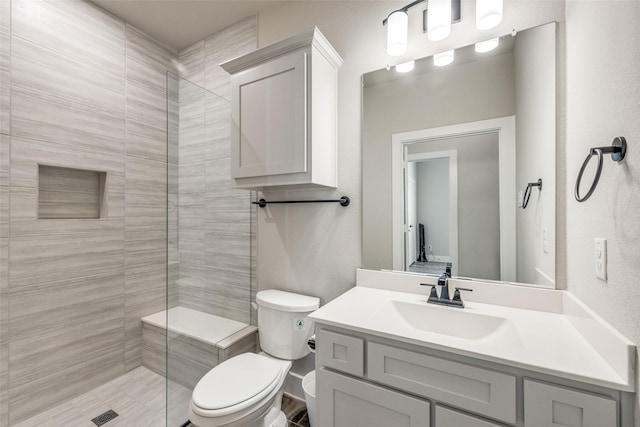 full bathroom featuring a tile shower, toilet, and vanity