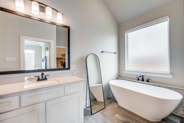 bathroom with vaulted ceiling, plenty of natural light, a soaking tub, and vanity