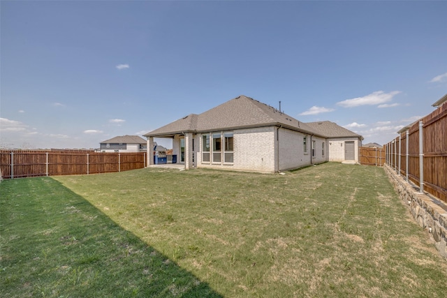 back of house featuring brick siding, a yard, a patio area, and a fenced backyard