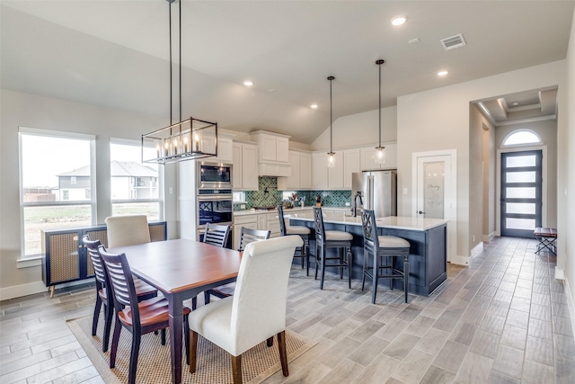 dining space with an inviting chandelier, vaulted ceiling, visible vents, light wood-type flooring, and baseboards