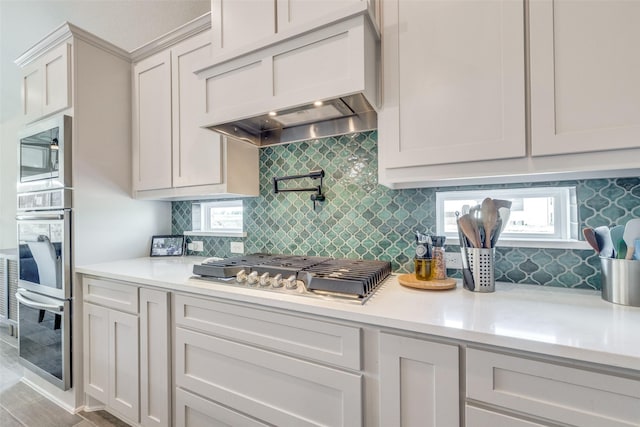 kitchen with light countertops, tasteful backsplash, appliances with stainless steel finishes, and premium range hood