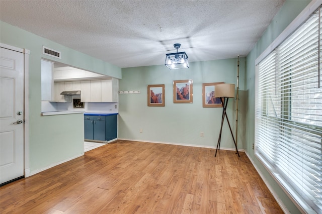 unfurnished dining area featuring light wood-type flooring, baseboards, visible vents, and a textured ceiling