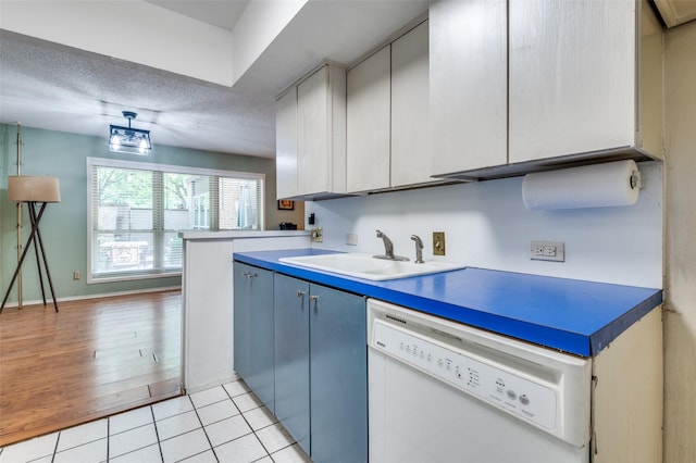 kitchen featuring white dishwasher, a sink, a textured ceiling, blue cabinets, and light tile patterned floors