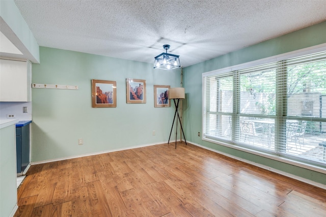 empty room with an inviting chandelier, light wood-style floors, a textured ceiling, and baseboards