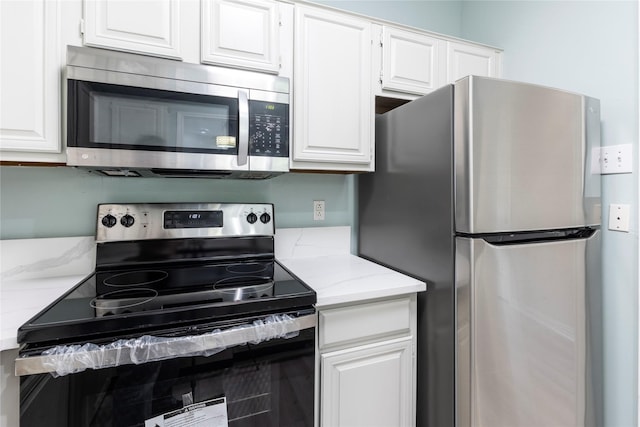 kitchen with white cabinets, appliances with stainless steel finishes, and light stone counters