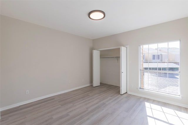 unfurnished bedroom featuring baseboards, light wood finished floors, and a closet