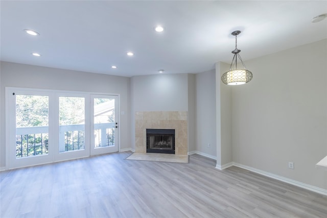 unfurnished living room with a tiled fireplace, baseboards, recessed lighting, and light wood-style floors