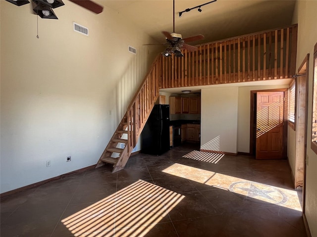 unfurnished living room featuring a ceiling fan, visible vents, and a high ceiling