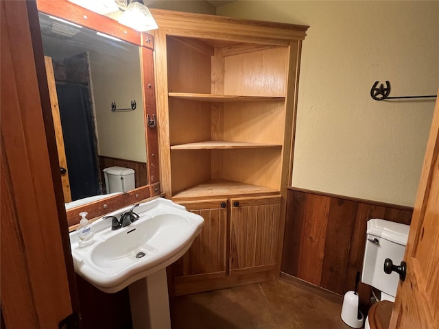 bathroom with wooden walls, toilet, a wainscoted wall, and a sink