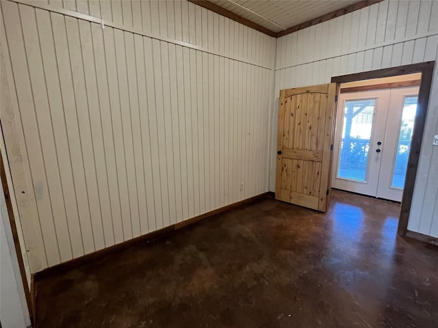 foyer entrance with wood walls, french doors, baseboards, and concrete floors