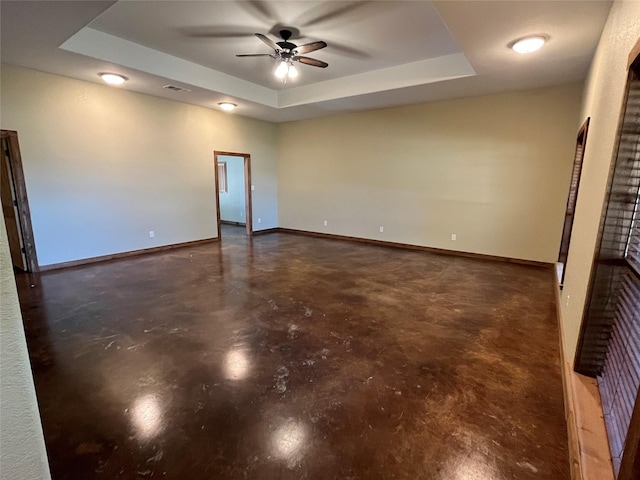 empty room featuring baseboards, a ceiling fan, a tray ceiling, and finished concrete flooring