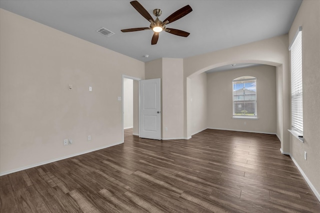 spare room with a ceiling fan, arched walkways, dark wood-type flooring, and baseboards