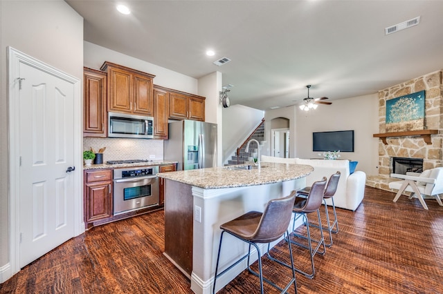 11529 Penick Way, Frisco, TX 75033 - kitchen featuring appliances with stainless steel finishes, light stone counters, dark wood-style flooring, a ceiling fan, and a kitchen breakfast bar