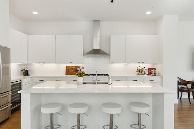 kitchen with wall chimney range hood, decorative backsplash, a kitchen bar, and a sink