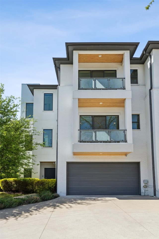 view of front of home with brick siding, a garage, stucco siding, a balcony, and driveway