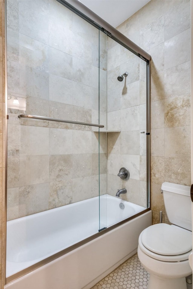 bathroom with tile patterned flooring, toilet, bath / shower combo with glass door, and tile walls