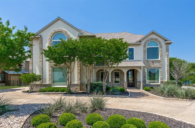 view of front of property with stucco siding, a porch, stone siding, and a shingled roof