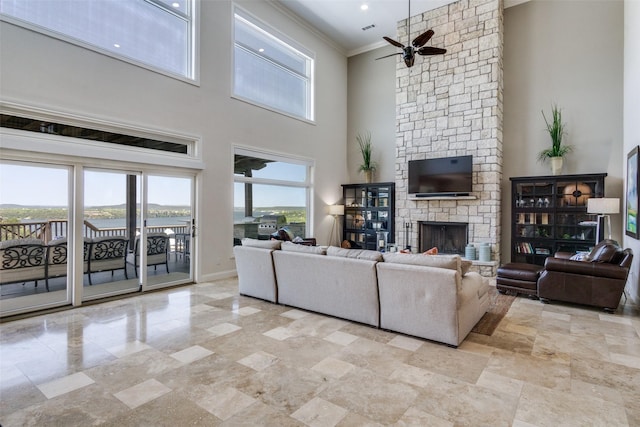 living room with crown molding, ceiling fan, baseboards, a fireplace, and a high ceiling