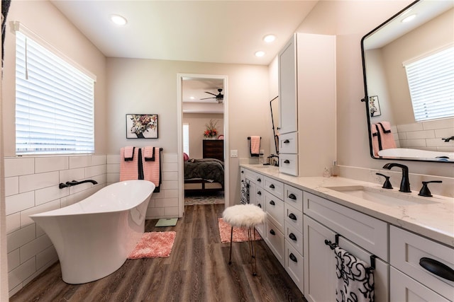 full bath with a soaking tub, wood finished floors, and a sink