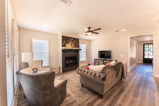 living area with a tiled fireplace, wood finished floors, visible vents, and ceiling fan