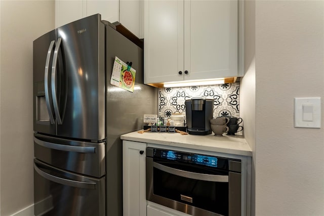 kitchen featuring white cabinets, oven, stainless steel fridge, tasteful backsplash, and light stone countertops