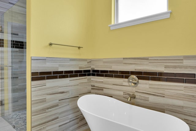 full bath featuring a shower stall, a freestanding tub, a wainscoted wall, and tile walls