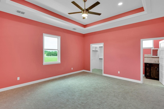 unfurnished bedroom with a tray ceiling, visible vents, light colored carpet, and multiple windows