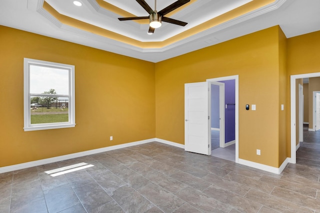 spare room with a raised ceiling, crown molding, baseboards, and ceiling fan