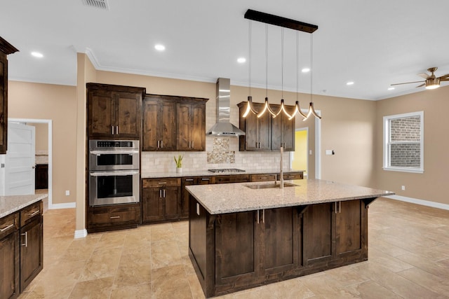 kitchen featuring stainless steel appliances, wall chimney range hood, a sink, light stone countertops, and decorative backsplash
