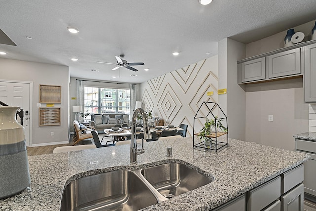 kitchen featuring light stone counters, wood finished floors, gray cabinets, a sink, and ceiling fan