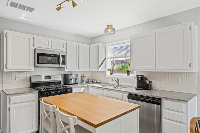 kitchen featuring visible vents, white cabinetry, stainless steel appliances, and a sink
